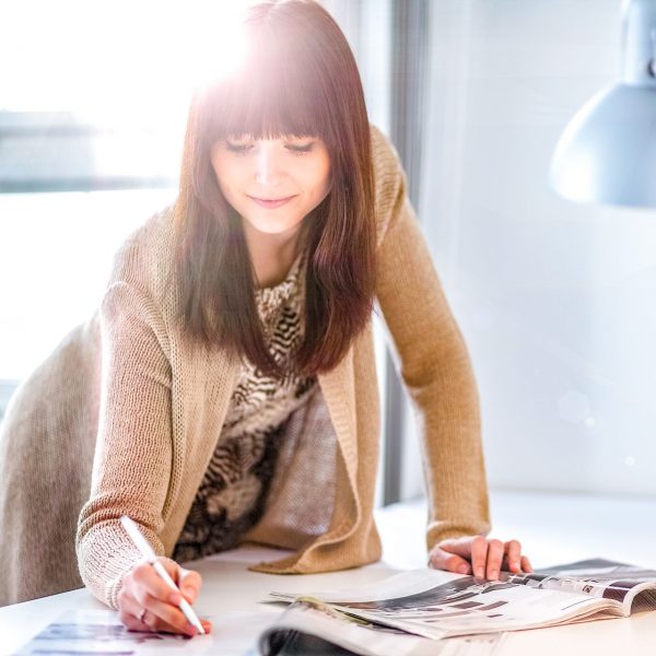 A business woman leaning over her desk and writing on a piece of paper with the sun shining in the background
