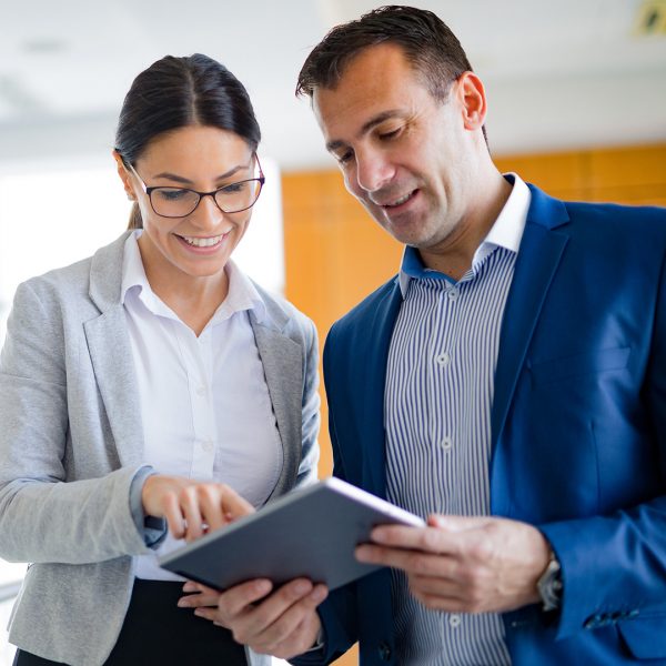 Woman and man collaborate while looking down at a tablet smiling